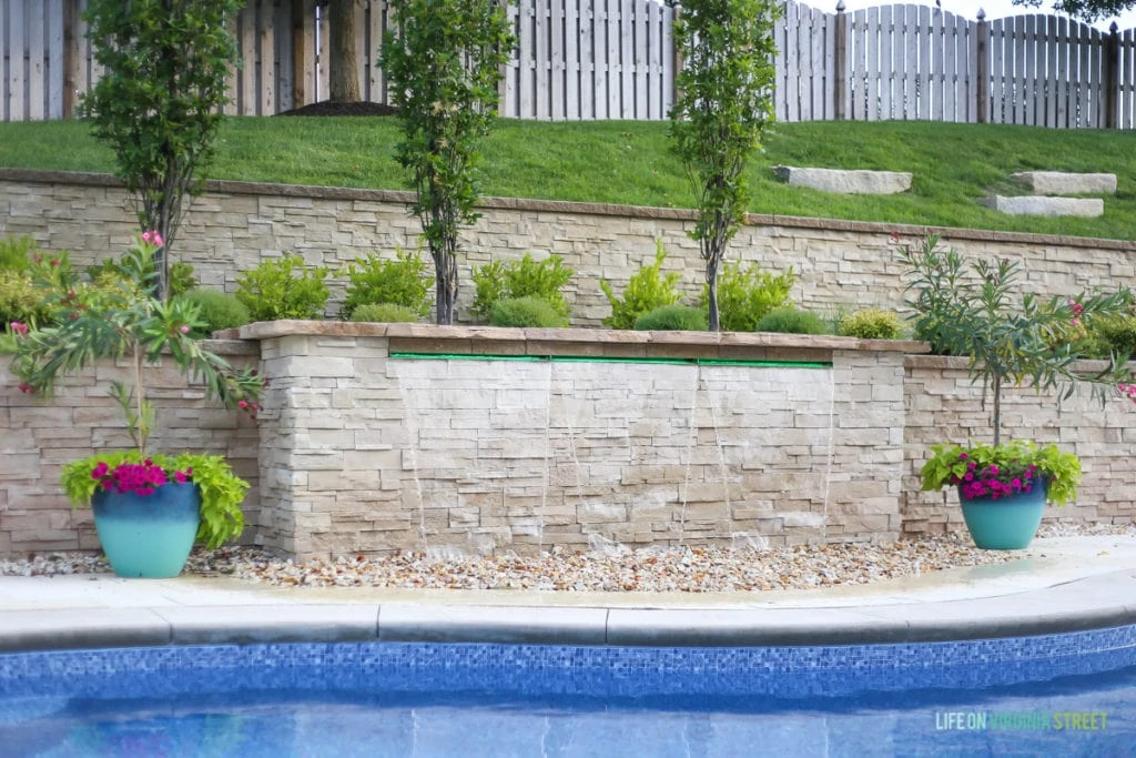 An inground pool with a rock retaining wall and planters beside the pool.