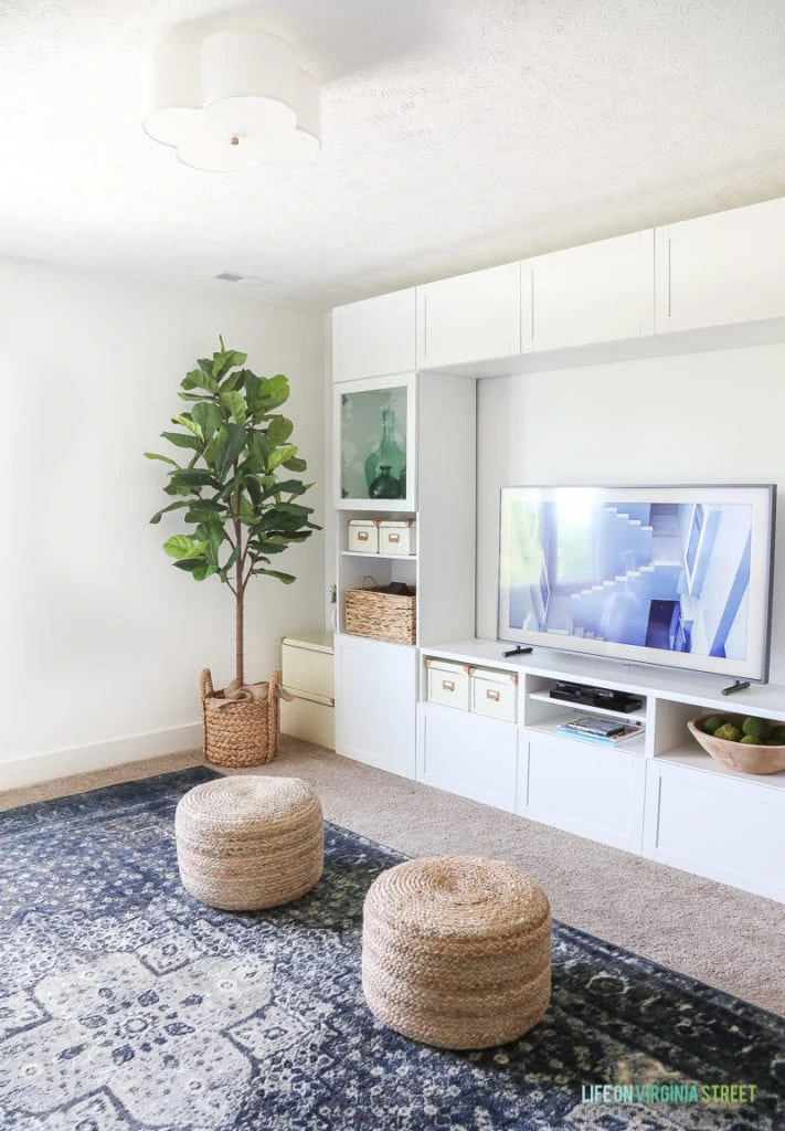 Completely blown away by this TV that looks like art (The Frame from Samsung). Also loving this craft room / TV room painted in Benjamin Moore Simply White. The IKEA BESTA stores fabric and other crafts, and the navy blue rug, fig tree and sisal poufs add color and texture. The white scalloped flushmount light fixture is perfection! #ad
