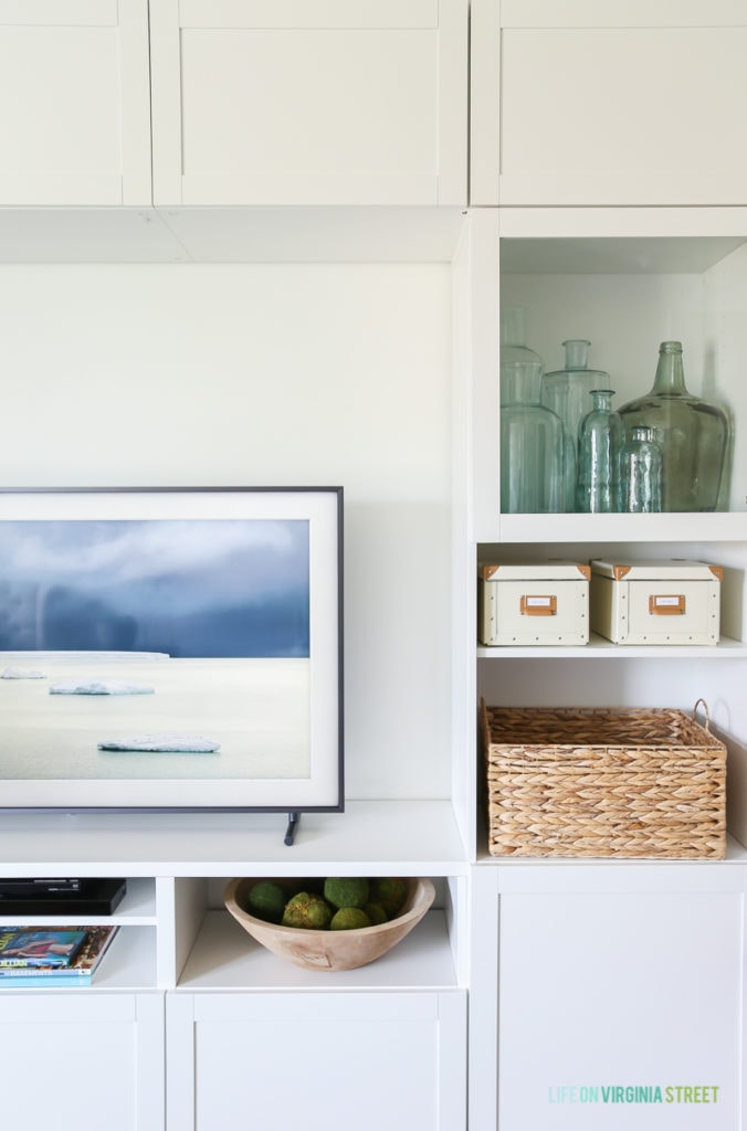 Completely blown away by this TV that looks like art (The Frame from Samsung). Also loving this craft room / TV room painted in Benjamin Moore Simply White. The IKEA BESTA stores fabric and other crafts, and the navy blue rug, fig tree and sisal poufs add color and texture. The blue and green recycled glass bottles are so pretty here! #ad