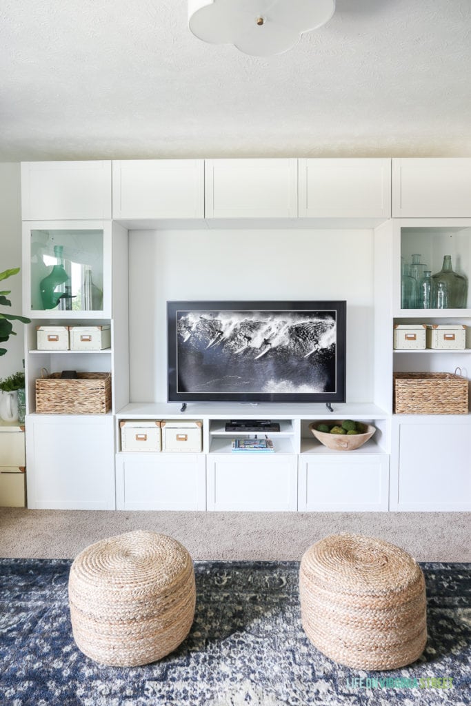 Check out this TV that looks like art (The Frame from Samsung). TV room painted in Benjamin Moore Simply White. The IKEA BESTA stores fabric and other crafts, and the navy blue rug, fig tree and sisal poufs add color and texture. The white scalloped flushmount light fixture is perfection! #ad