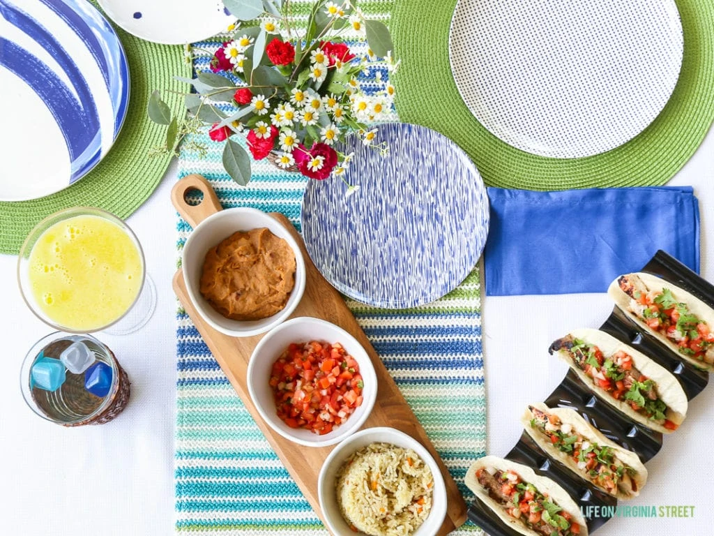 Salsa, guacamole on a wooden board, and tacos half made with flowers on the outdoor table.