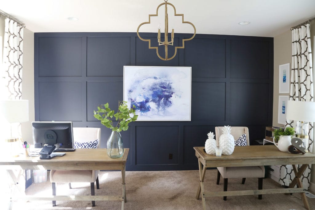 An office with two desks, a blue/gray wall behind the desks with abstract art on the wall.