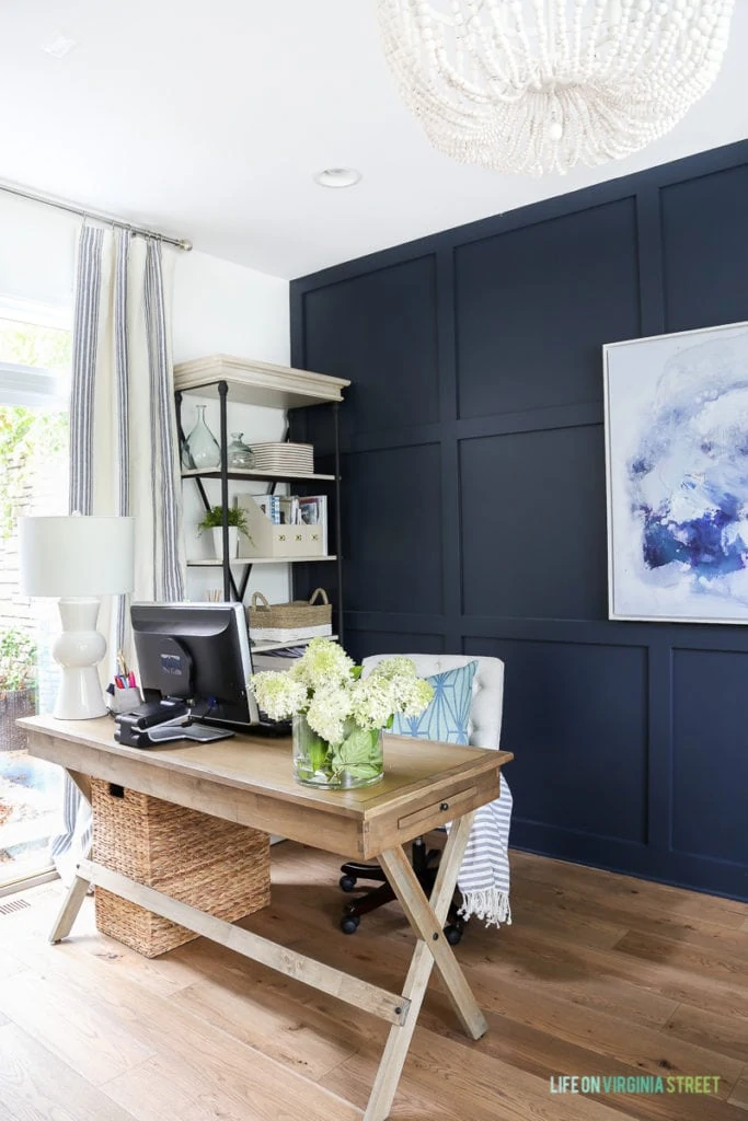 A light wooden desk, navy blue wall in the background and an abstract picture on the wall. Sharing all the detail on how to hide computer cords and get your home office organized!
