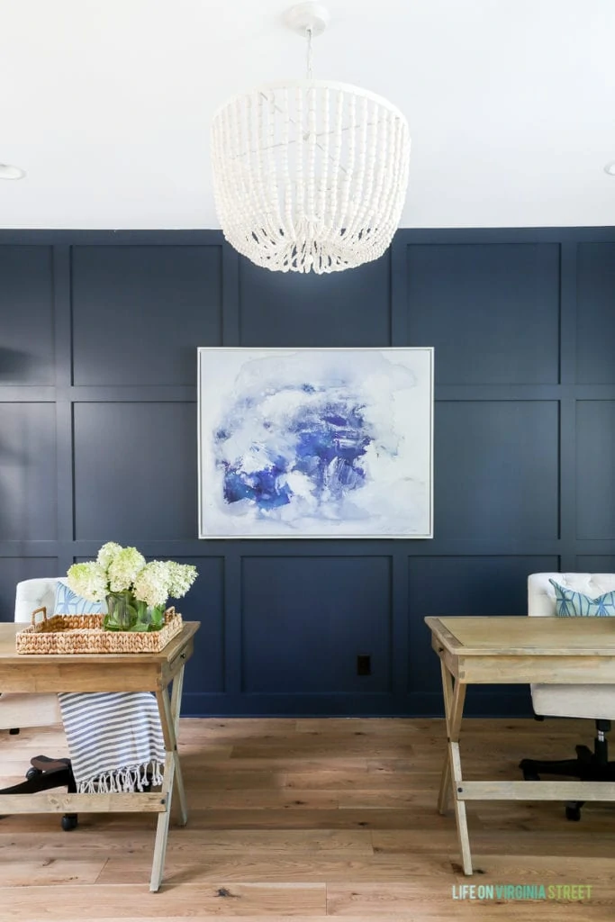 Two wooden desks in office and a white beaded chandelier above them centered. The board and batten walls are painted Benjamin Moore Hale Navy.