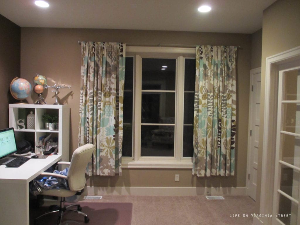 Carpeted office with desk and char and patterned curtains.