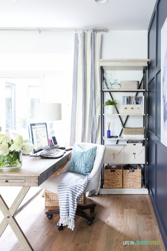 The office desk with a computer on it, a white office chair with a blue pillow and a striped blanket on it to.