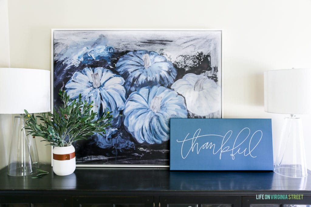 Blue pumpkin picture with a thankful card beside it and a vase filled with greenery.