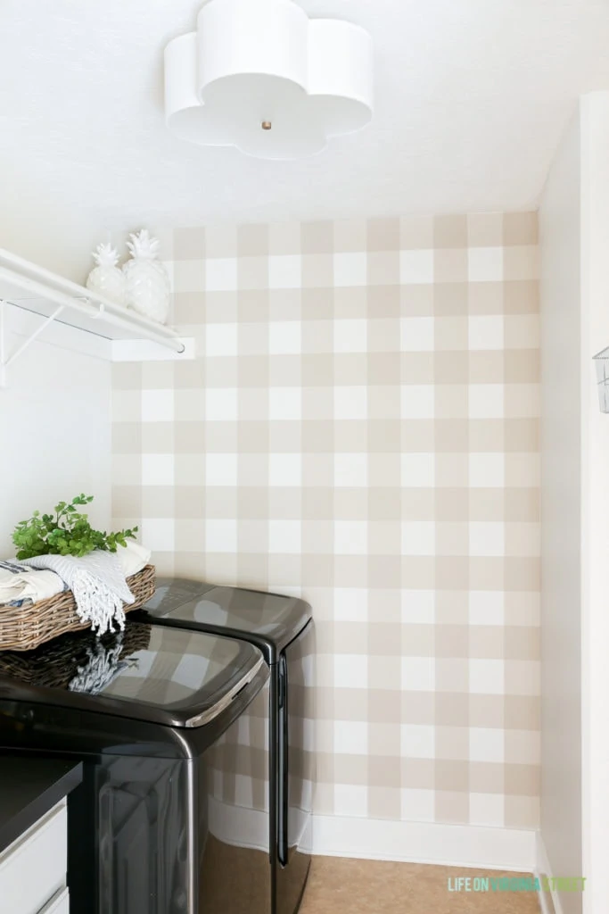 Laundry room with buffalo checks, a white shelf with white decorative pineapples on it, washer and dryer.