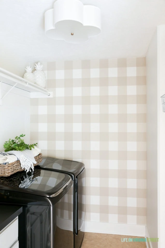 Beige and white buffalo checkered walls in laundry room with black washer and dryer pictured.