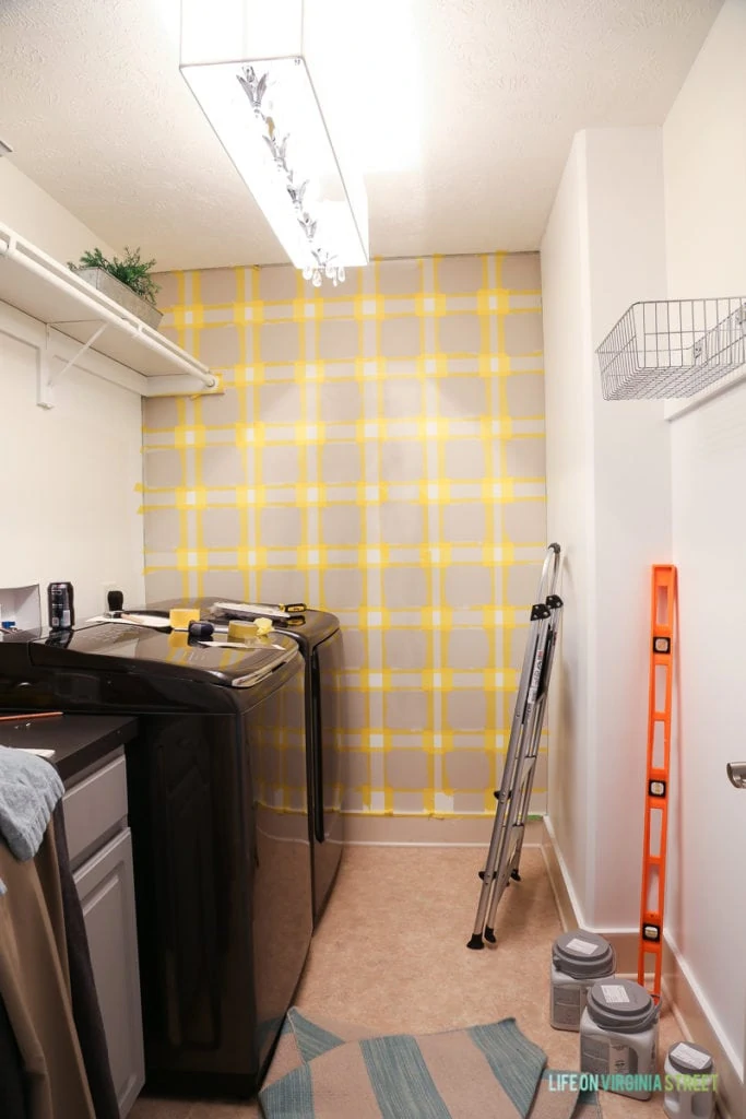 Taped walls in laundry room with step ladder and washer and dryer.