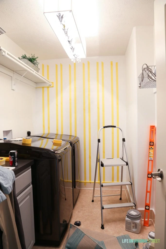 Rows of vertical yellow taped lines on wall in laundry room.