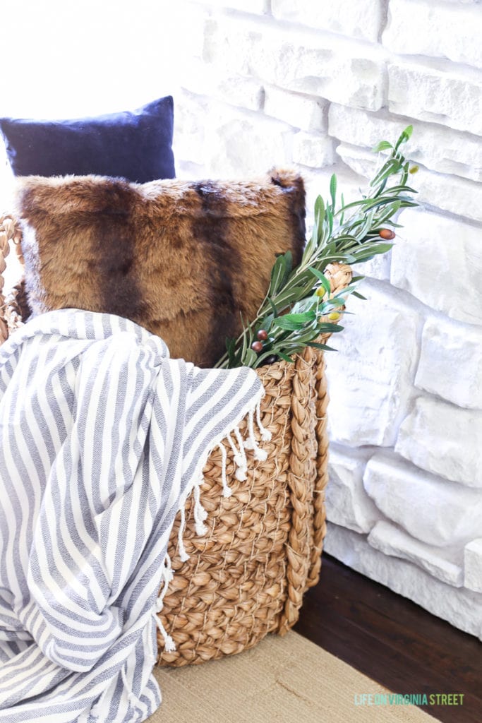 Hyacinth basket with navy blue velvet pillow, faux fur pillow, striped throw and olive leaf branch.