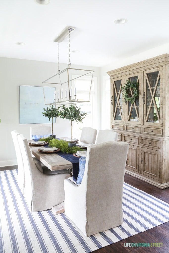 A blue and white striped rug, a wooden reclaimed table with fabric chairs.