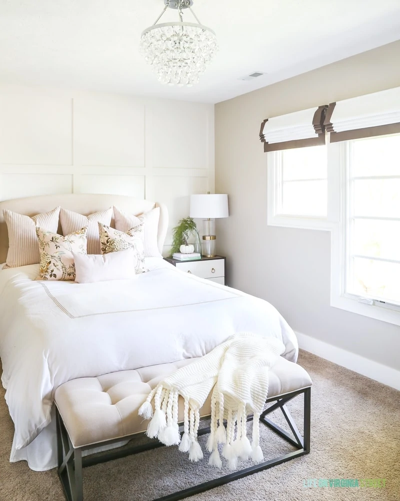 White neutral bed with bench at the foot of bed and a chandelier above.