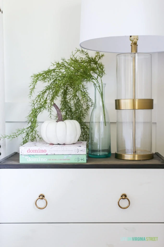 Side table with a white and gold lamp and a pumpkin on books.