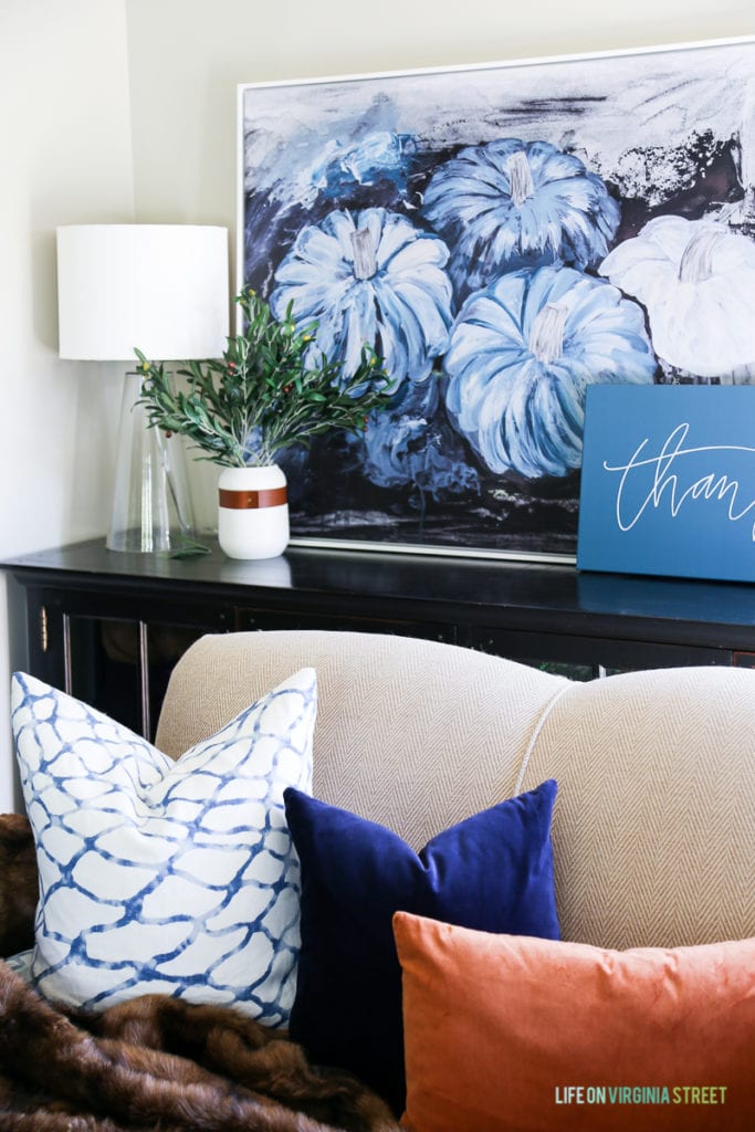 Gorgeous fall living room with navy blue, copper and neutrals. Loving the mix of velvet and faux fur. Also love the olive leaf branches, glass lamps, large blue pumpkins canvas art and 'thankful' canvas.