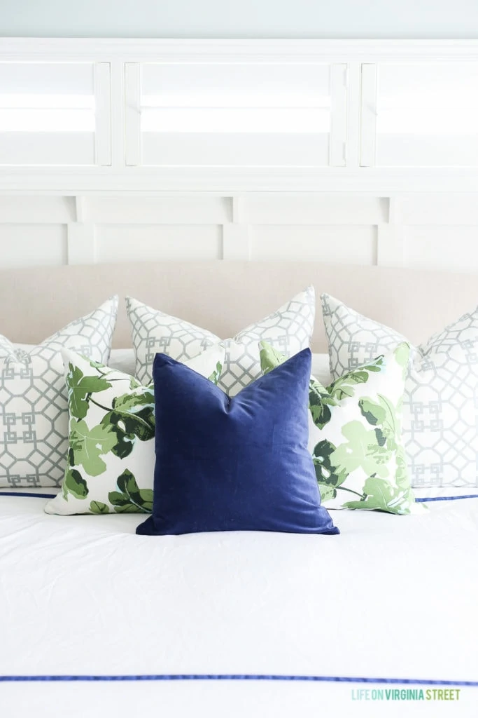 Linen headboard with white bedding, navy blue velvet pillow, fig leaf pillows, trellis pillows, white board and batten and Sherwin Williams Sea Salt walls.