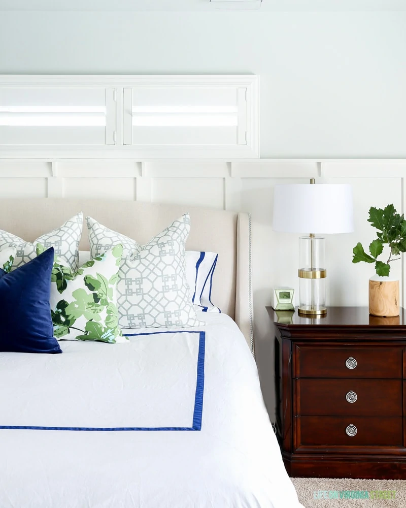 Master bedroom with white linens and blue and white pillows, Sherwin Williams Sea Salt Walls, navy blue velvet pillow, fig leaf pillows, trellis pillows, white board and batten and oak leaves.
