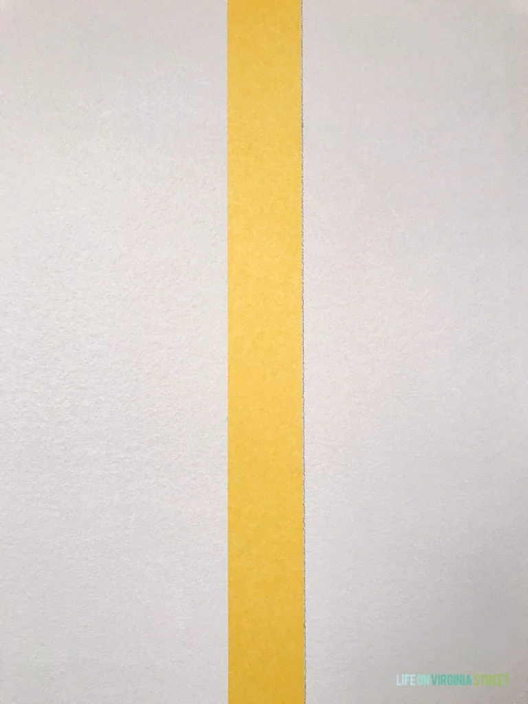 Pencil line beside the yellow tape on wall in laundry room.