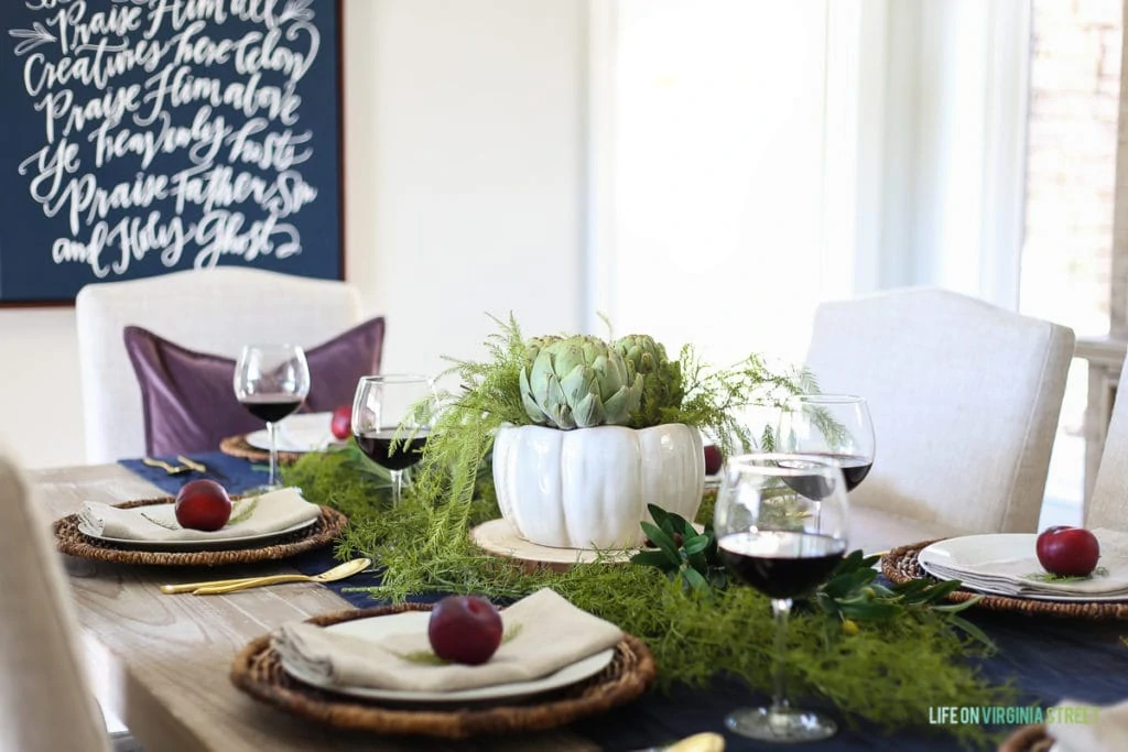 Plates set on table with a plum on each plate and an artichoke as the centrepiece.