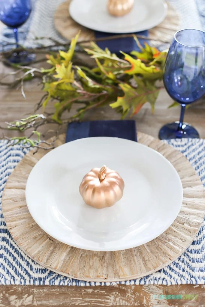 A blue Thanksgiving place setting with driftwood chargers and woven blue and white placemats and blue wine glasses.