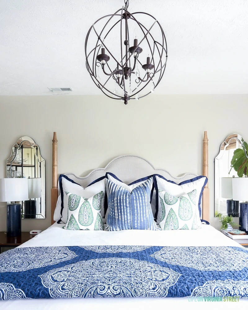 Mirror in corner, lamps on side tables, chandelier, and blue and white bedding in room.