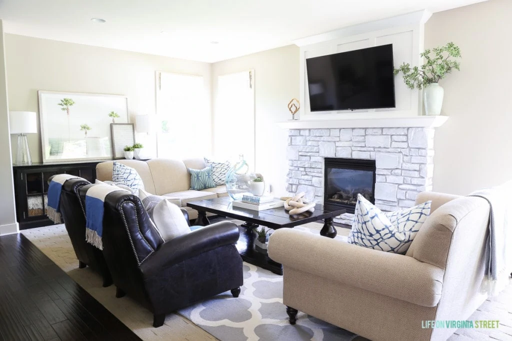 Living room chairs, a white brick fireplace, a tv above the fireplace, and a blue and white rug.