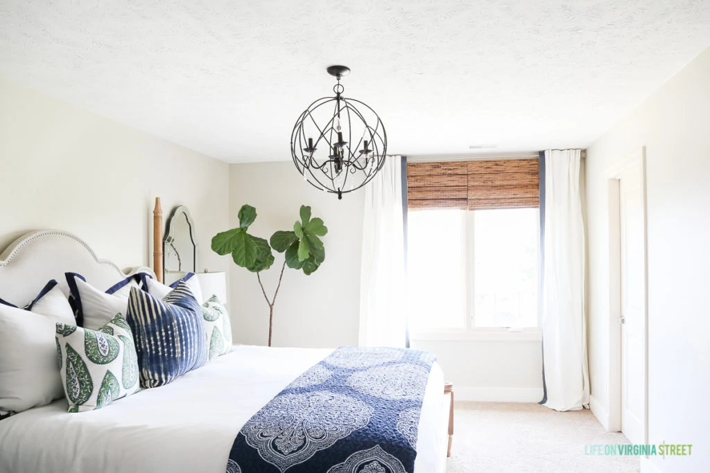 White neutral walls, a large window, a chandelier and bed in the guest bedroom.