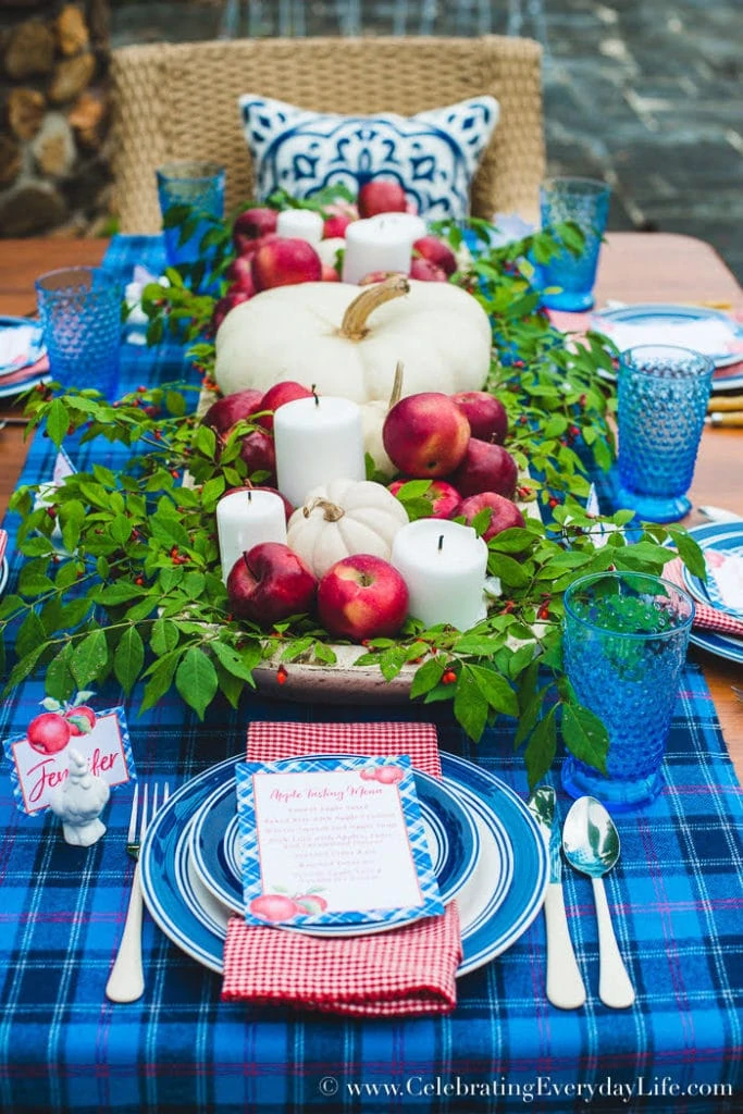 A blue plaid table runner with apples, candles and pumpkins as the centrepieces.