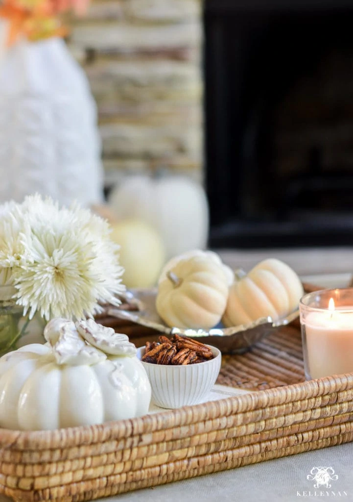 A wicker tray with white pumpkins, toasted pecans, and white flowers on it.