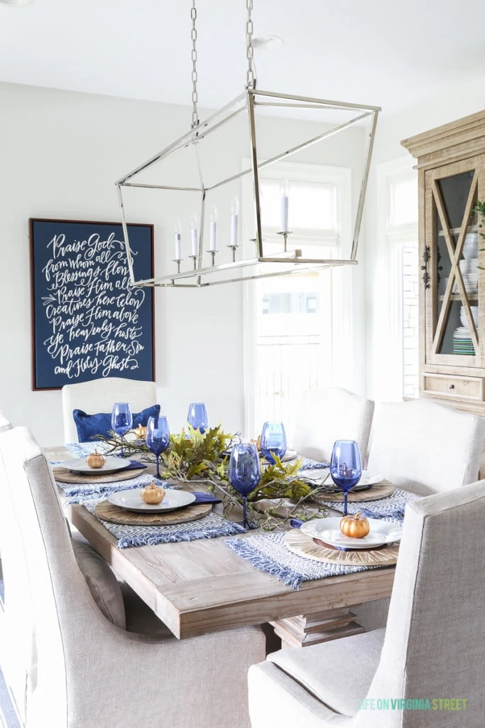 Blue and white Thanksgiving dining room with navy blue doxology canvas, Darlana linear pendant, blue wine glasses, reclaimed wood table, and linen chairs.