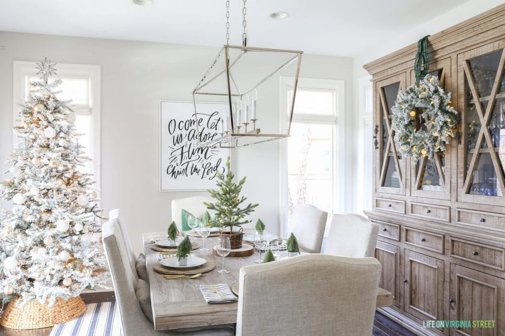 A dining room table with a flocked Christmas tree in the corner of the room. The table is decorated in a woodland theme.