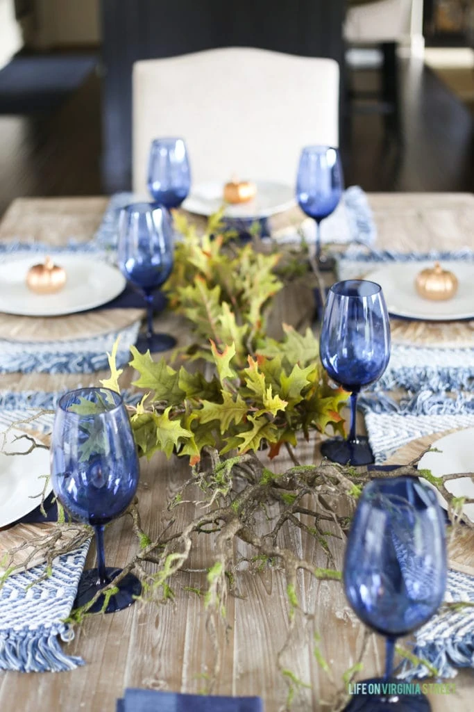 Touches of greenery add life to driftwood charges and bright blue glasses in this gorgeous Thanksgiving tablescape. 