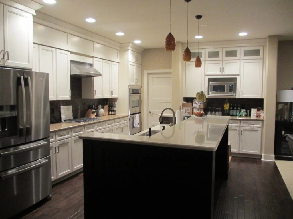 White cabinets, a white topped island and pendant lights in the kitchen.