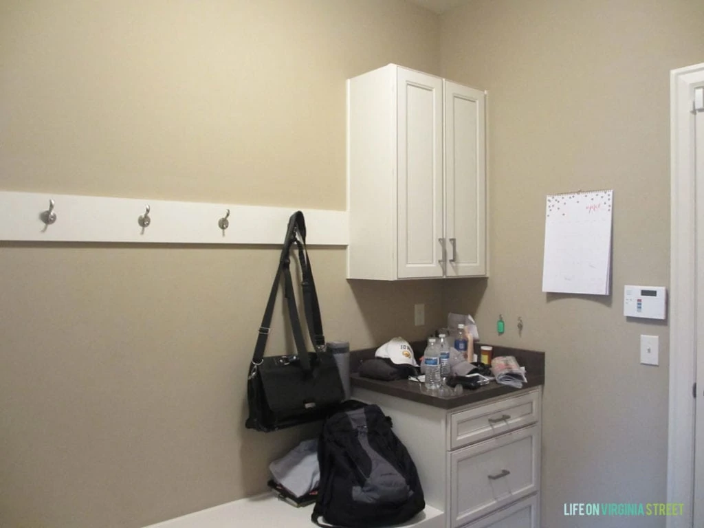 The mudroom with a small cabinet and drawers and hooks on the wall, plus a small white bench.