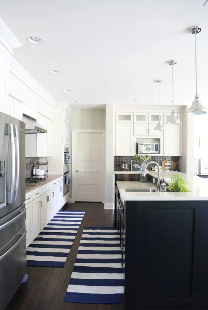 White kitchen with a black island and dark oak hardwood floors and striped blue and white runner rugs.
