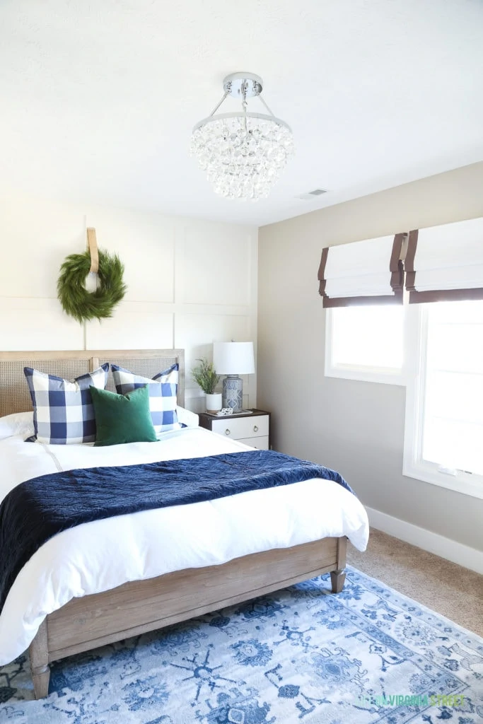 Blue and white bedroom with a crystal chandelier, driftwood color bed, white and navy blue bedding and buffalo check pillows.