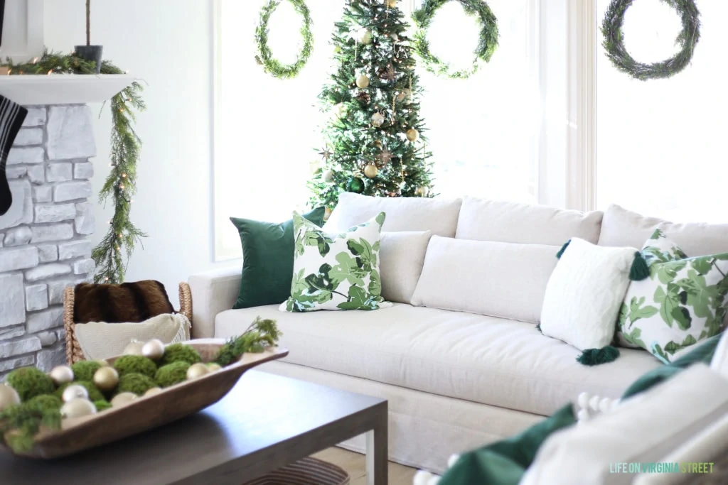 Linen slip-covered sofa with dark green velvet pillow and fig leaf pillows. Christmas tree with gold, brown and dark green ornaments.