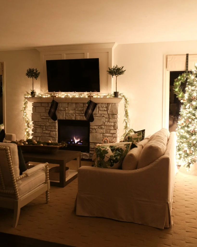 Fireplace lit in living room, with two stockings hanging on it, and a decorated mantel.
