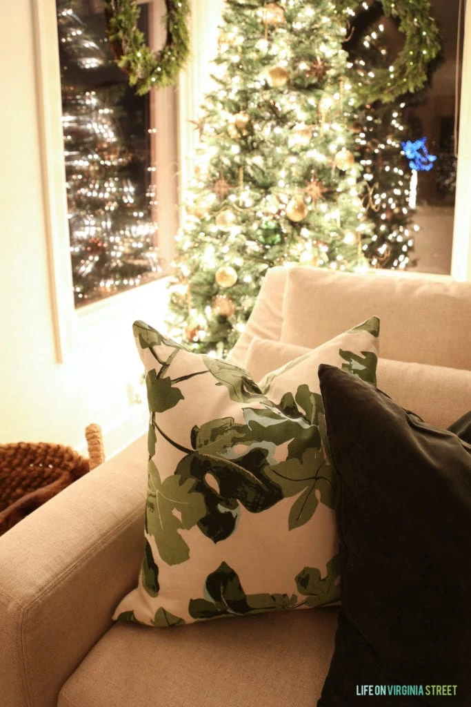 Green and white pillow on couch, with Christmas tree behind it.