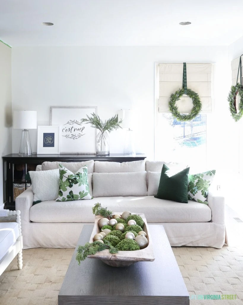 Christmas living with a linen York Slope Arm Sofa from Pottery Barn. I love the dark green velvet and fig leaf pillows and the wreaths on the windows! Large dough bowl filled with ornaments and greenery. The artwork is from Lindsay Letters. So perfect for the holidays!