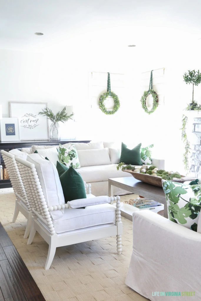 Christmas living room painted Benjamin Moore Simply white with white spindle chairs and linen York Slope Arm Sofas from Pottery Barn. I love the dark green velvet and fig leaf pillows and the wreaths on the windows! So perfect for the holidays!