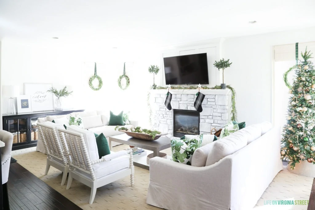 The same living room pained white with a white brick fireplace and white furniture and the room decorated for Christmas.