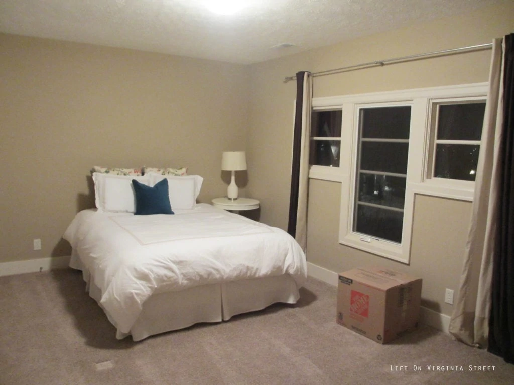 The guest bedroom with off white walls, and a small white bed.
