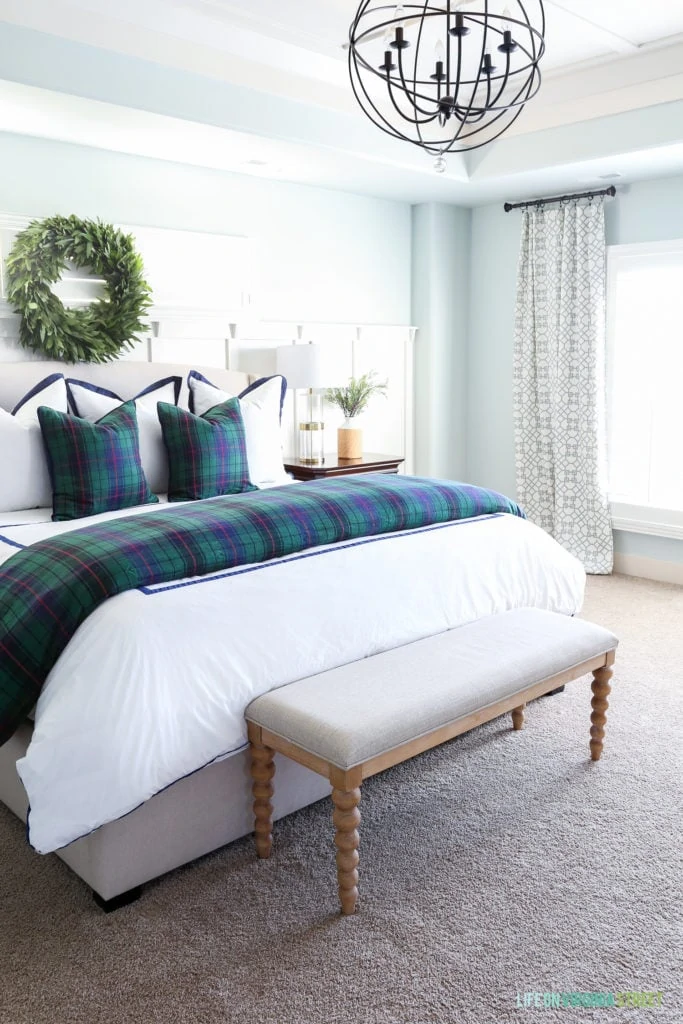 Christmas master bedroom with navy blue and green plaid bedding, tartan pillows, orb chandelier and a fresh bay leaf wreath over the bed.