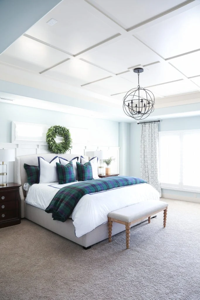 Christmas bedroom with Sherwin Williams Sea Salt walls, navy blue and green tartan bedding, board and batten trayed ceiling, and a fresh bay leaf wreath over the bed.