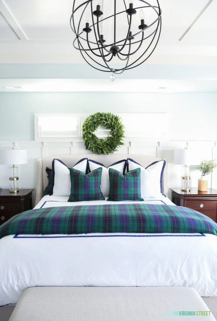 Christmas bedroom with fresh green wreath, white duvet, tartan bedding, and gold and glass lamps.