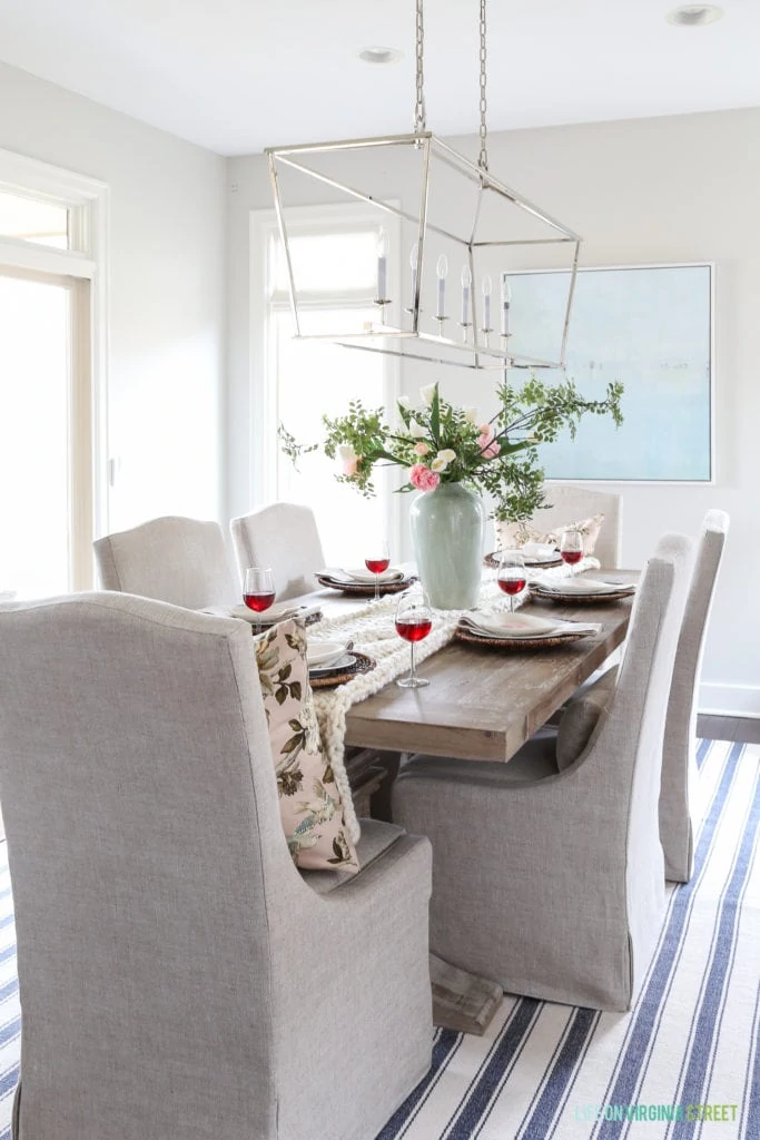 Dining room table set for Valentine's Day with red wine in glasses, a striped rug and pendant light fixture.