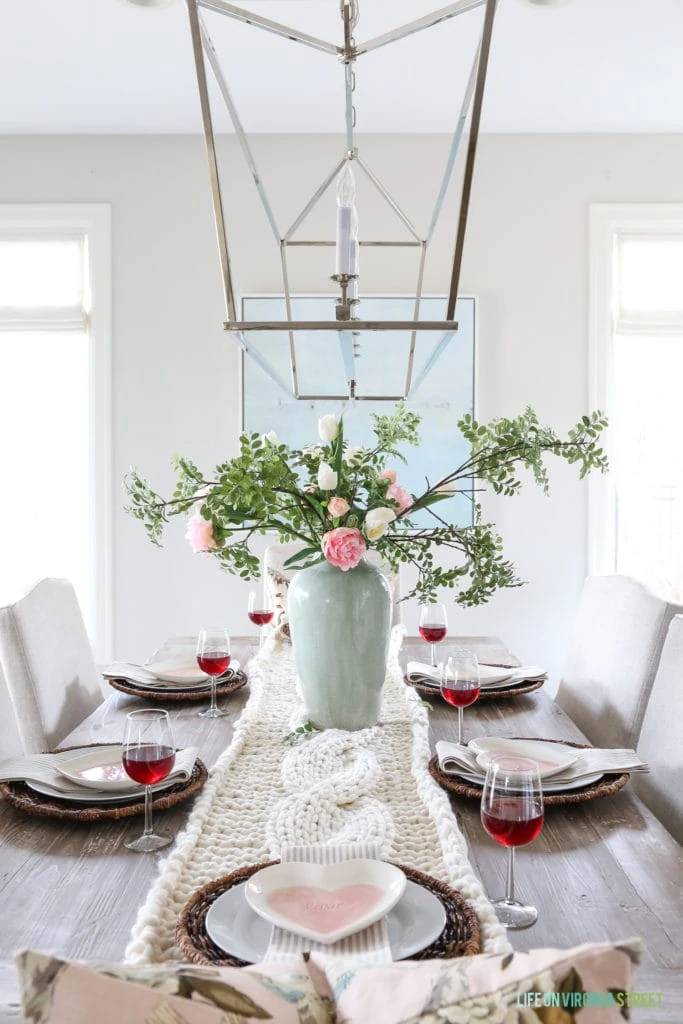 Valentine's Day table with heart shaped plates, striped napkins, chunky knit throw table runner and peony and tulip centerpiece.