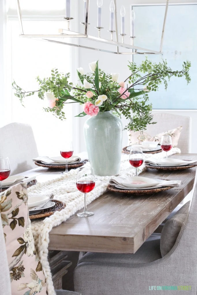 A light pink  peony and greenery in a white vase on the table.